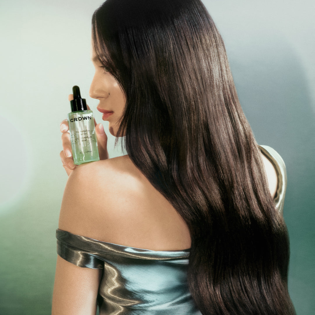 Woman with long, shiny hair holding a bottle of hydrating hair oil.